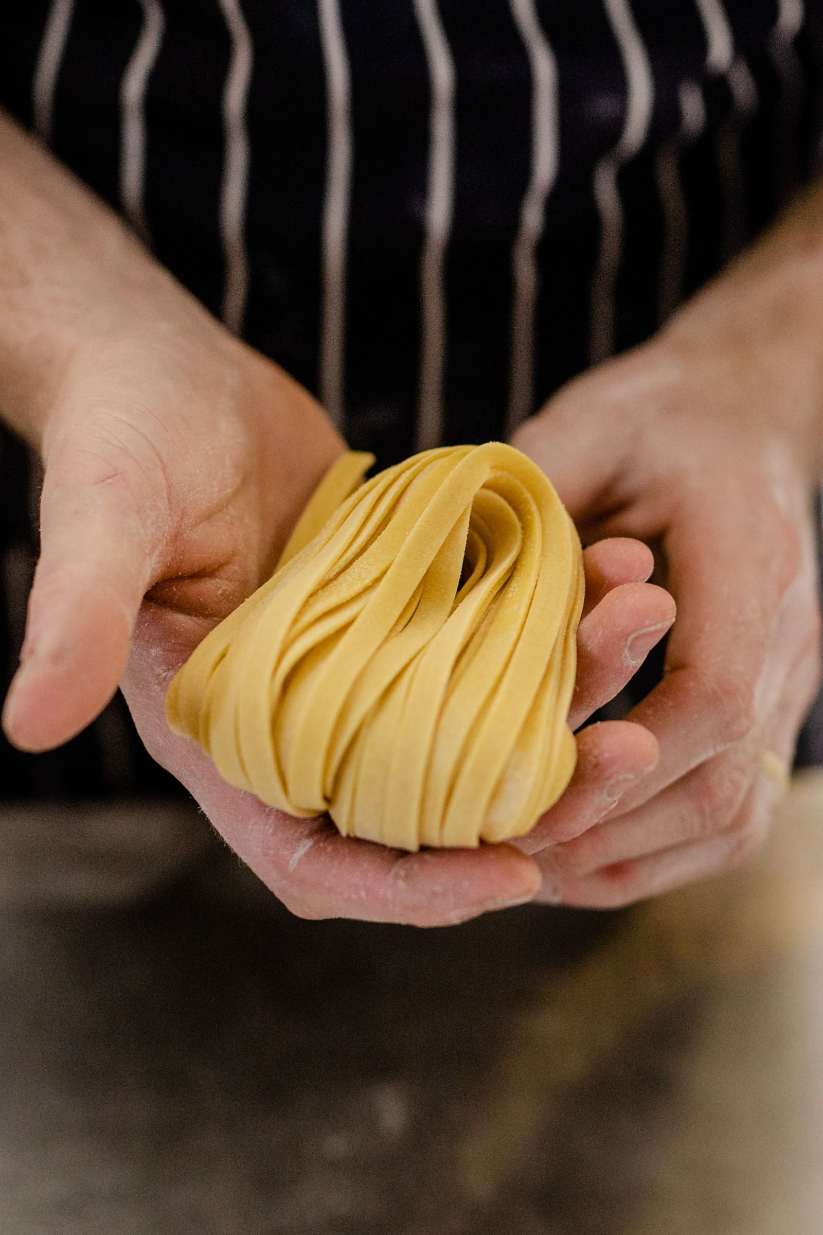 An amount of fresh tagliatelle being held by a chef