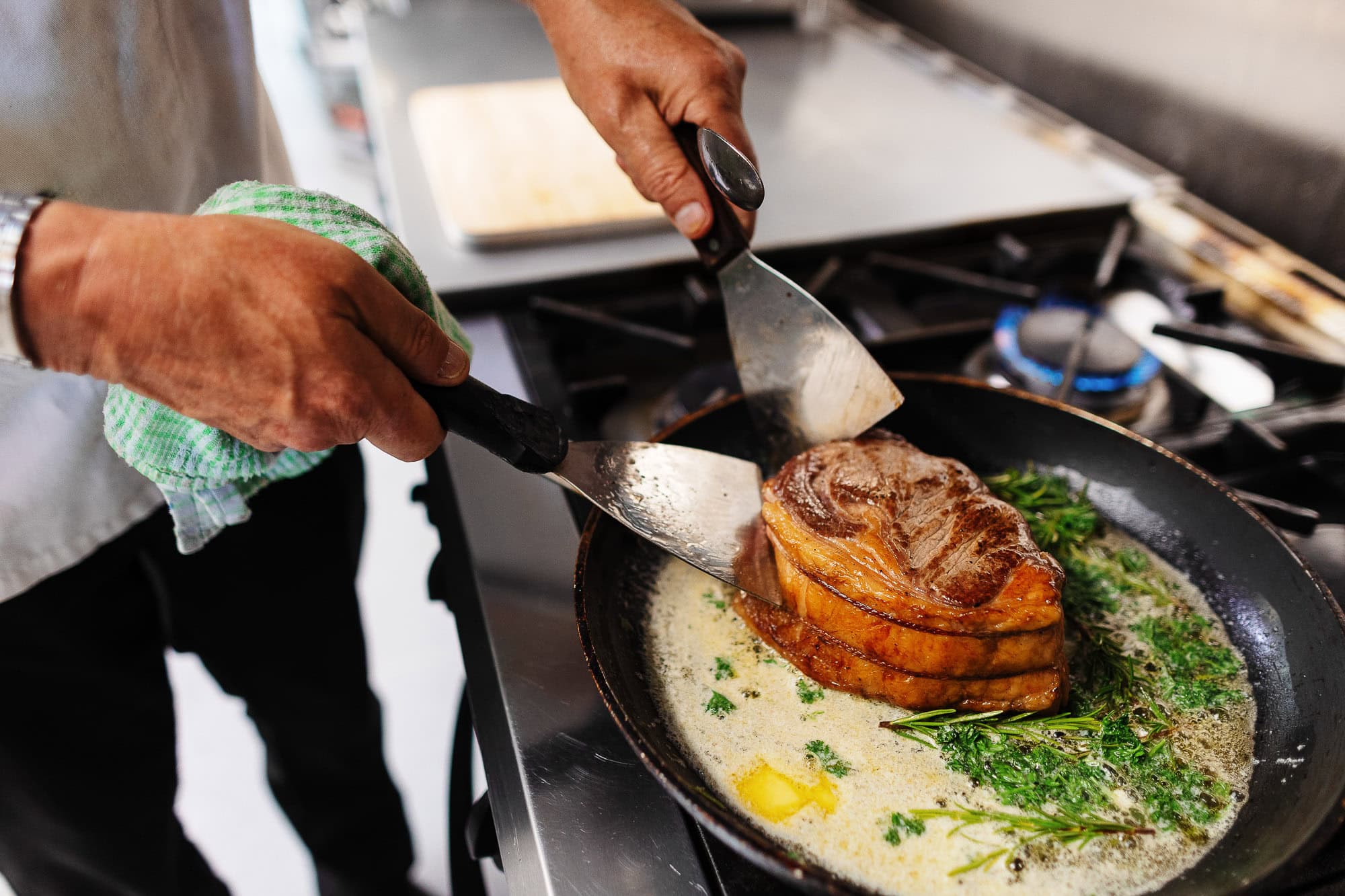 Succulent steak being cooked in a skillet with fresh herbs and butter, highlighting professional food preparation and culinary skills.