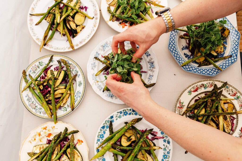 Vibrant vegetarian dish featuring grilled asparagus, courgettes, and fresh herbs arranged on vintage floral plates for food photography.