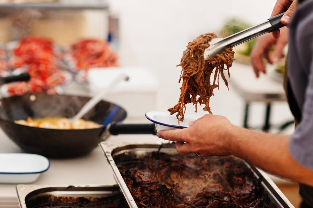 Slow-cooked shredded beef being served into a bowl at a culinary event in Rutland, UK.
