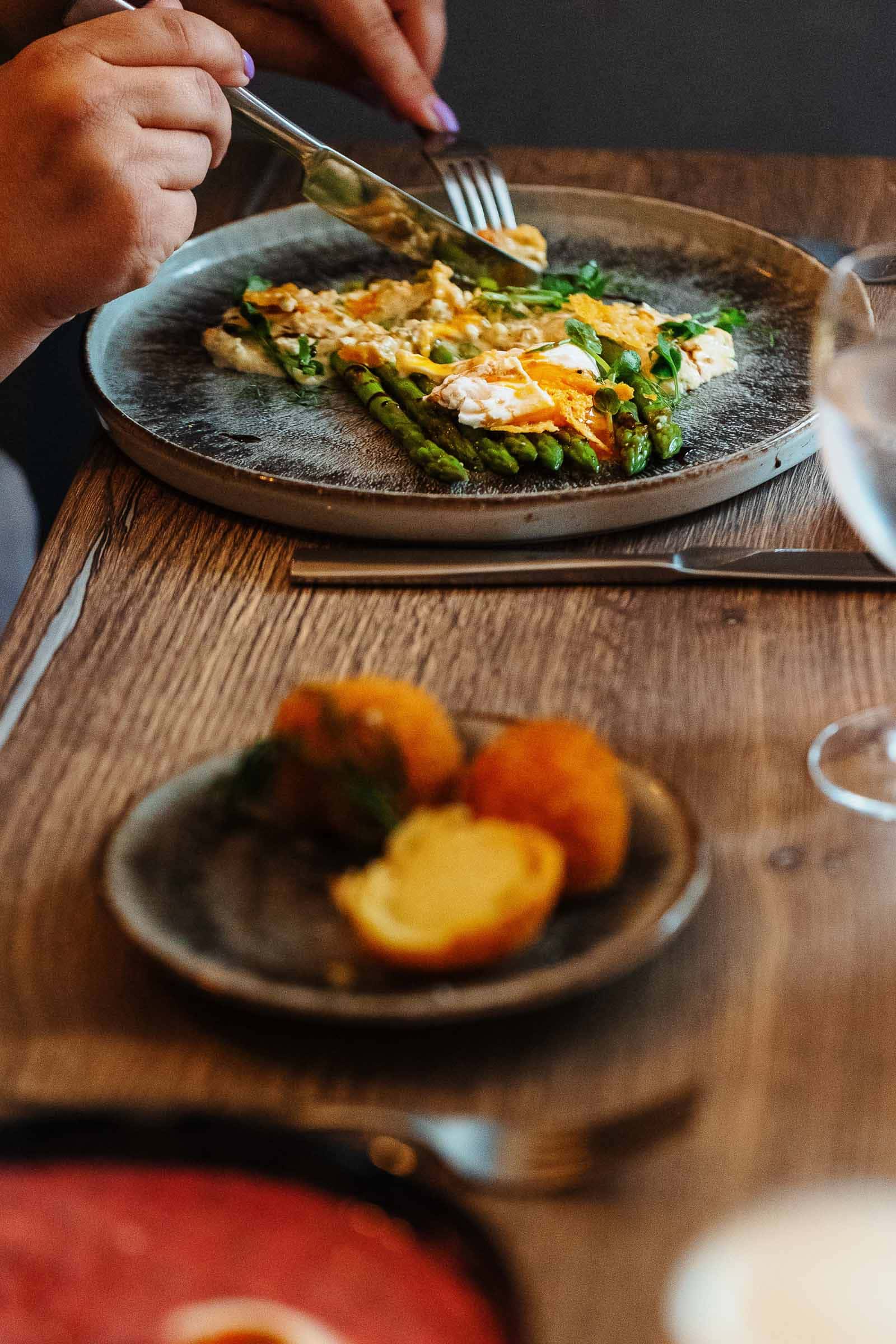 A plate of asparagus and poached egg being eaten with a knife and fork