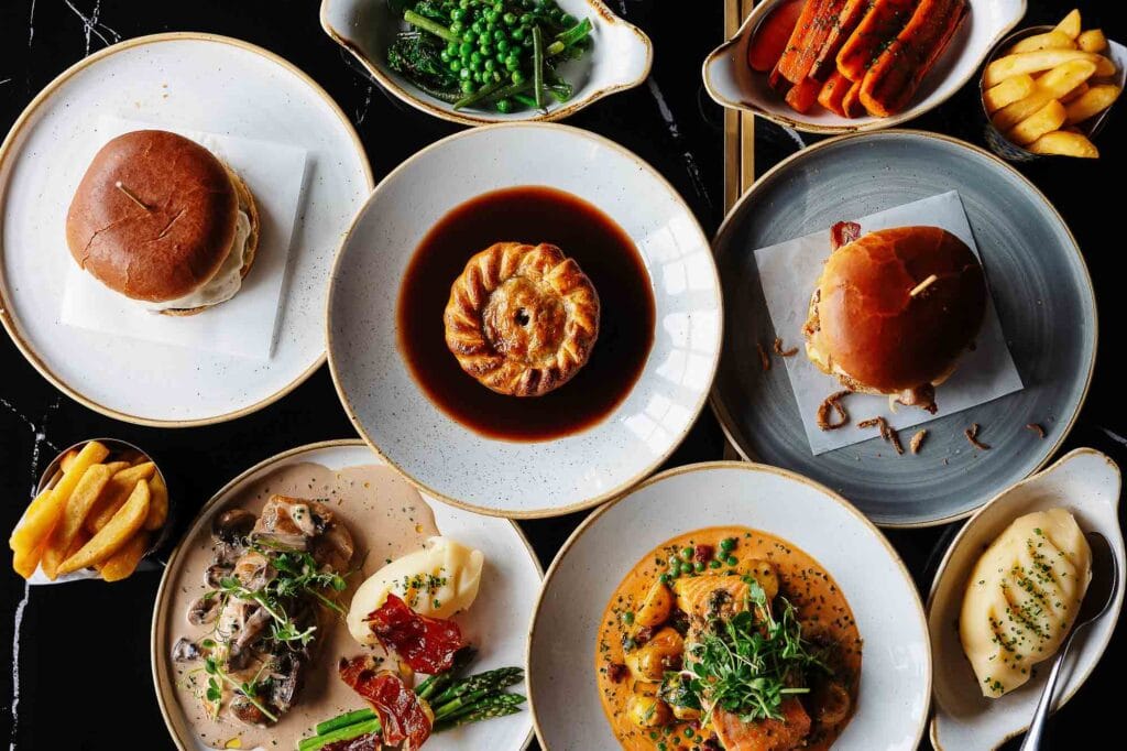 Colorful British-inspired food dishes including burger with bun, pastry, mashed potatoes, vegetables, and sauces, professionally plated for a gourmet food photography shoot in Rutland.