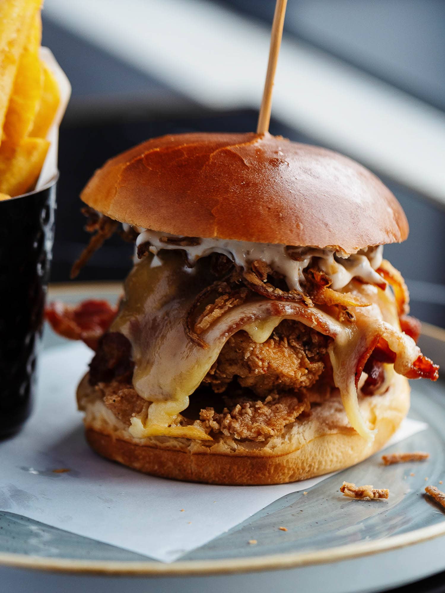Juicy gourmet burger with crispy bacon, melted cheese, shredded onions, and a brioche bun, served with golden fries. Perfect for food photography and showcasing delicious UK comfort food.