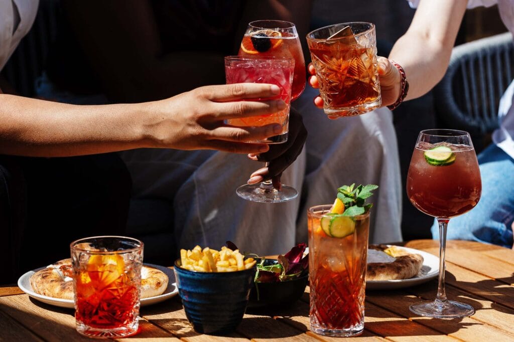 Vibrant cocktails and pizza share a lively outdoor dining scene captured by Rutland food photographer, highlighting colourful drinks and social atmosphere.
