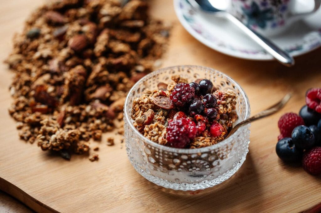 Crunchy granola with mixed berries in a glass bowl on a wooden surface.