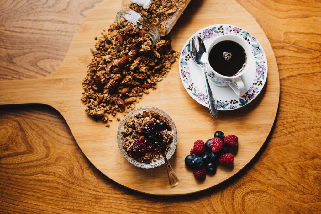 Delicious breakfast with granola, fresh berries, and a cup of black coffee on a wooden serving board. Perfect food photography captured by Rutland food photographer for appealing food presentation.