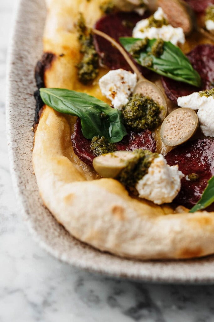 Crispy crust pizza with pepperoni, basil, mozzarella, and green pesto on marble surface.