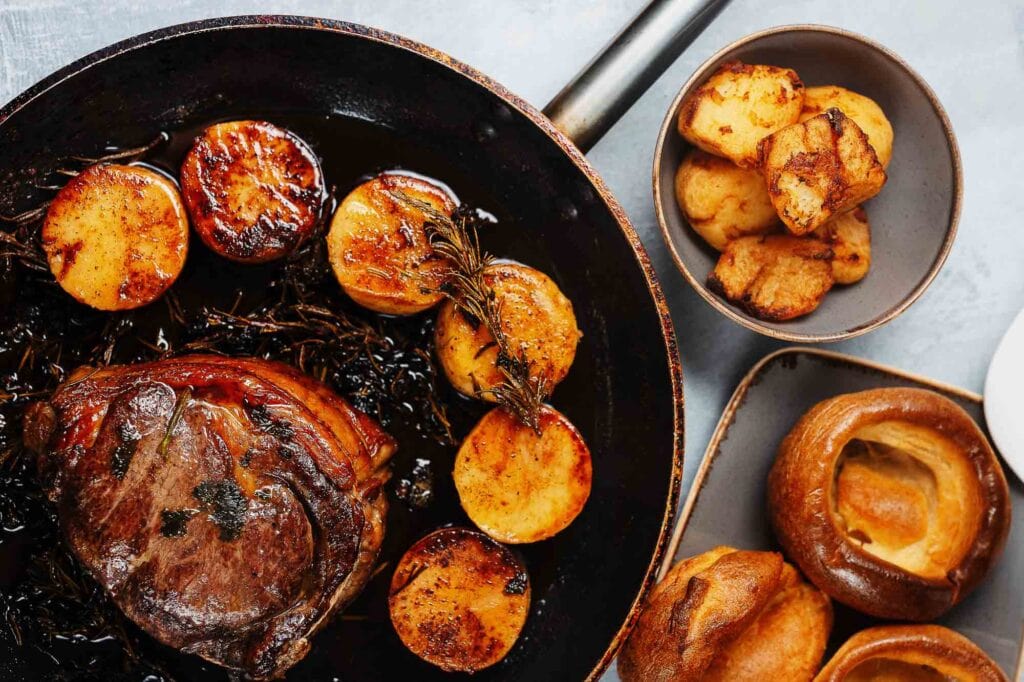 Succulent roast beef with crispy roasted potatoes and seasonal vegetables, served on a rustic black dish, perfect for food photography in Rutland.