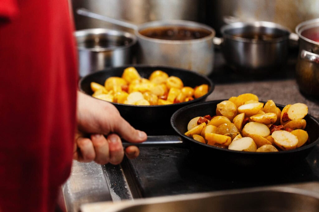 Roasted baby potatoes being cooked in a black frying pan in a professional kitchen.