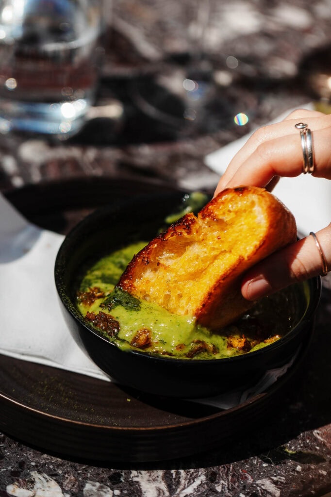 Crouton dipping into green soup with herbs, close-up of food photography, rustic outdoor dining, Rutland food photographer, professional food styling and capturing vibrant flavours.