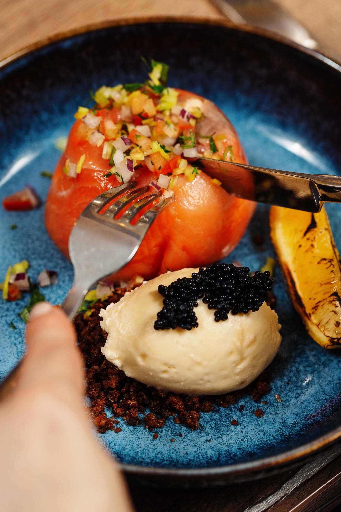 Freshly prepared baked tomato with chopped herbs and vegetables, served with smooth potato mash topped with black caviar, grilled lemon, on a rustic blue ceramic plate at a Rutland food photography session.