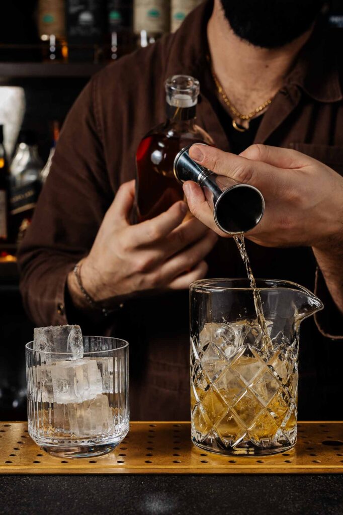 A professional food photographer capturing cocktail preparation with whiskey and ice, showcasing high-quality bar scene imagery for Rutland food photography and drink styling.