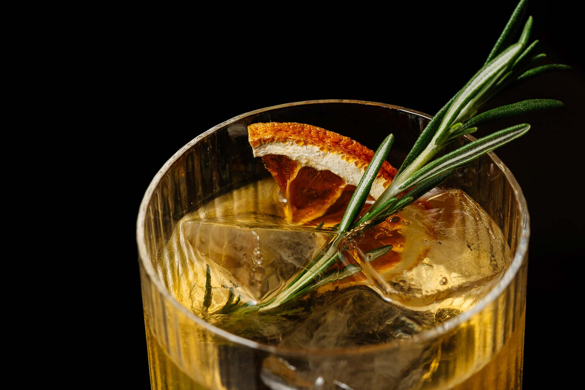 1. Elegant cocktail with orange slice and rosemary garnish in a crystal tumbler against black background for fine dining food photography.