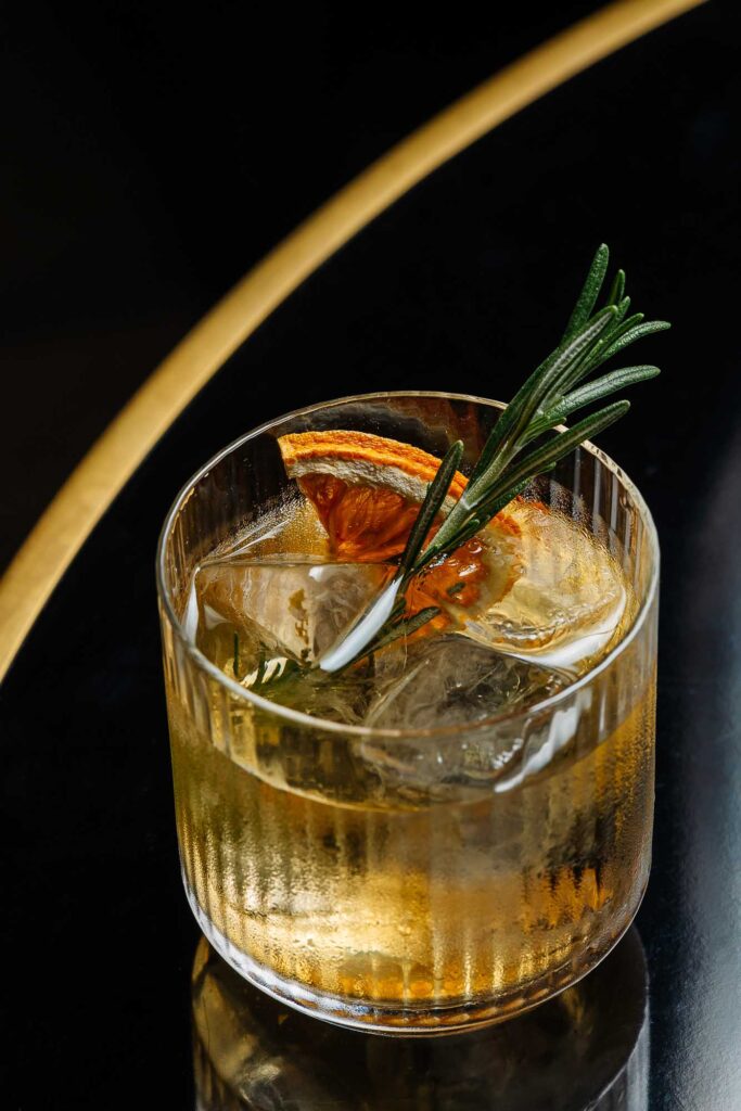 1. Close-up of a gin and tonic cocktail garnished with dried citrus slices and fresh rosemary, served in a short glass with ice, perfect for food photography in Rutland.