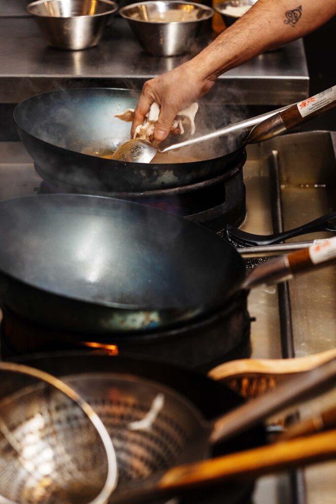 Frying in a commercial kitchen with woks and cooking utensils.