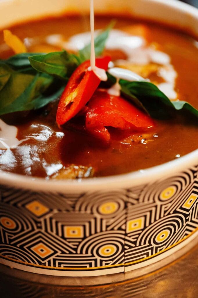 Delicious tomato soup garnished with fresh basil, sliced chili, and a drizzle of cream, served in a patterned bowl, perfect for food photography.