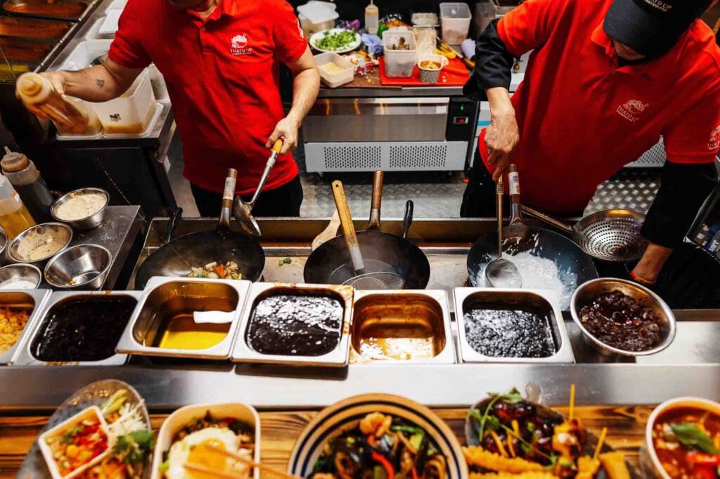 Professional chefs preparing diverse dishes in a bustling kitchen environment, showcasing fresh ingredients and cooking techniques.