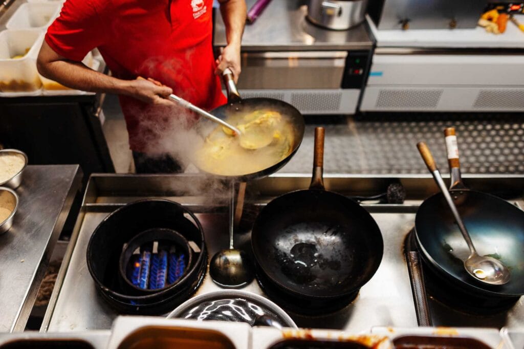 Chef cooking with a wok on a gas stove in a commercial kitchen, showcasing culinary skills and food presentation.