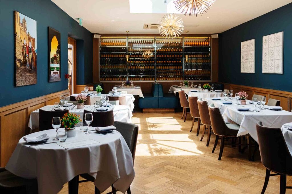 Stylish dining room featuring a wine wall, neatly arranged tables with white tablecloths, floral centrepieces, and modern decor, perfect for fine dining experiences in Rutland.