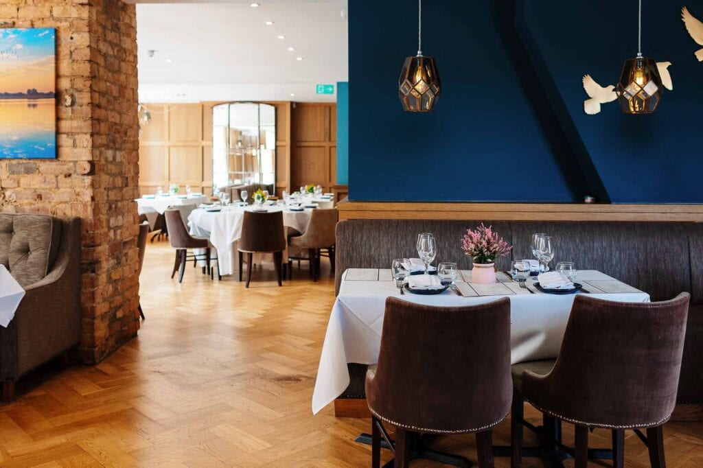 Charming restaurant interior featuring sophisticated decor, neatly arranged tables with white tablecloths, glassware, and floral centrepieces, perfect for a memorable dining experience.