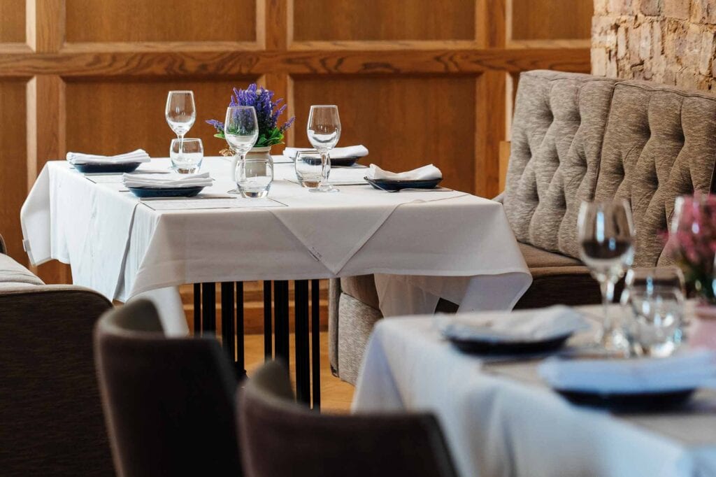 Stylish restaurant table with white linen, wine glasses, and floral centrepiece, perfect for fine dining in a cosy, rustic setting.