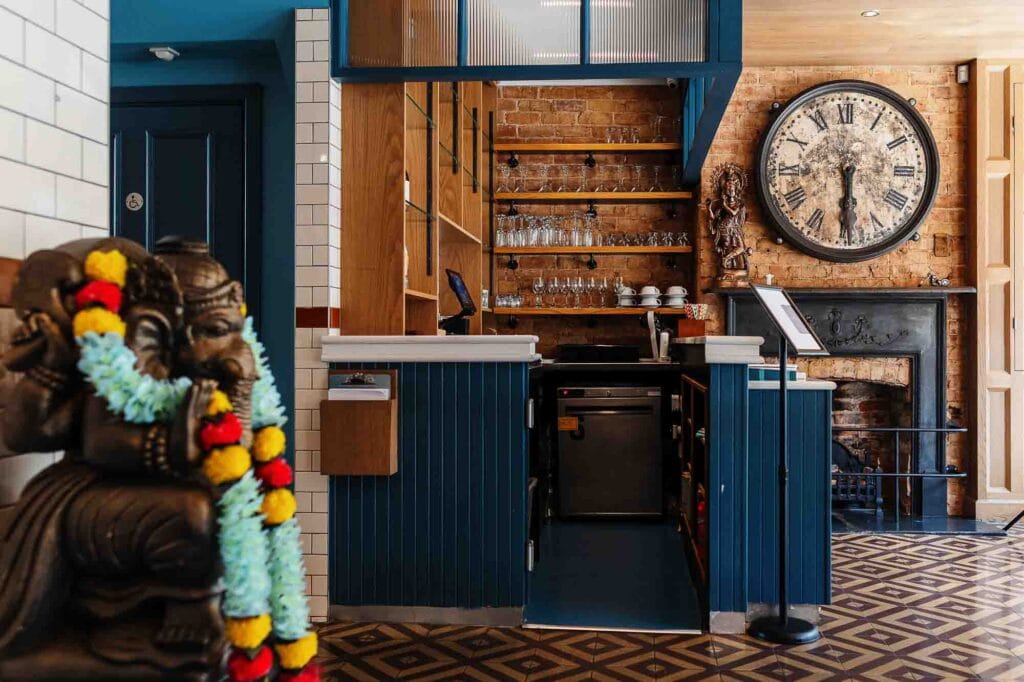 A stylish rustic bar interior featuring wooden shelves, a large vintage clock, and a cosy brick wall, perfect for food photography and capturing inviting hospitality settings.