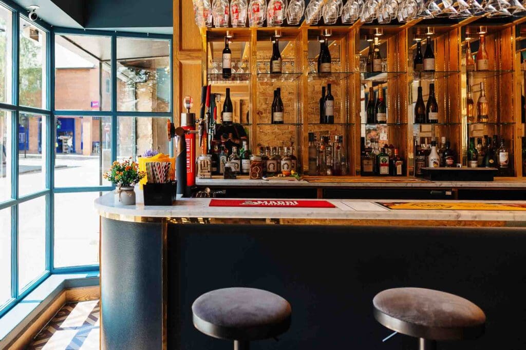 Bar interior with a variety of spirits and wine bottles displayed on wooden shelves, featuring a sleek counter and comfortable stools, ideal for food and drink photography in Rutland.