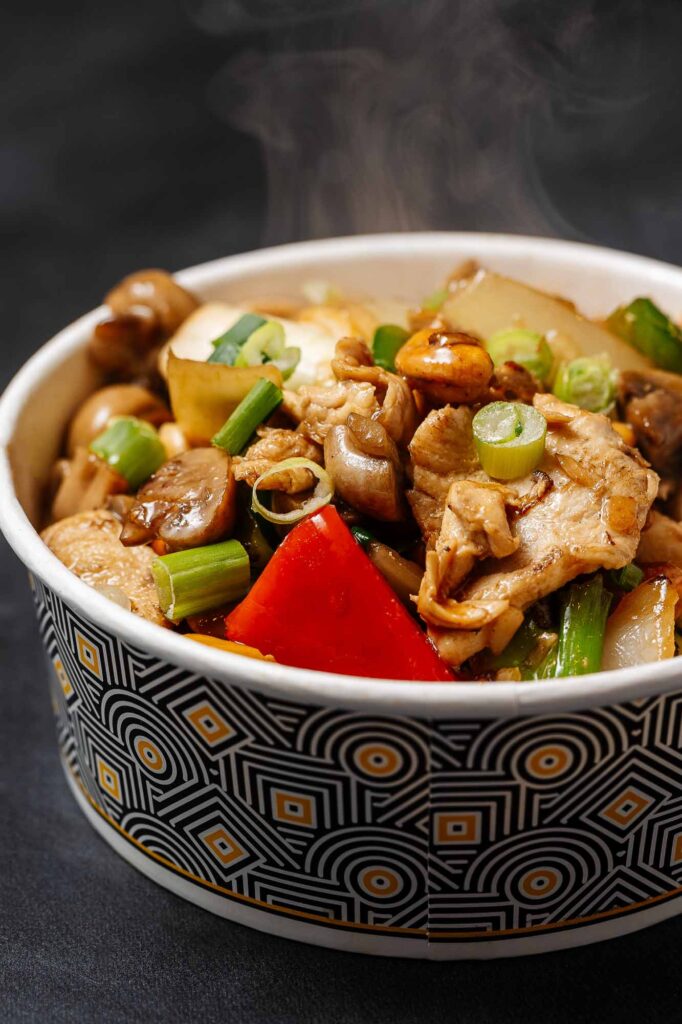 Delicious steaming Asian chicken and vegetable stir-fry in a patterned bowl, showcasing fresh ingredients like chicken, peppers, and green onions, perfect for a healthy meal.