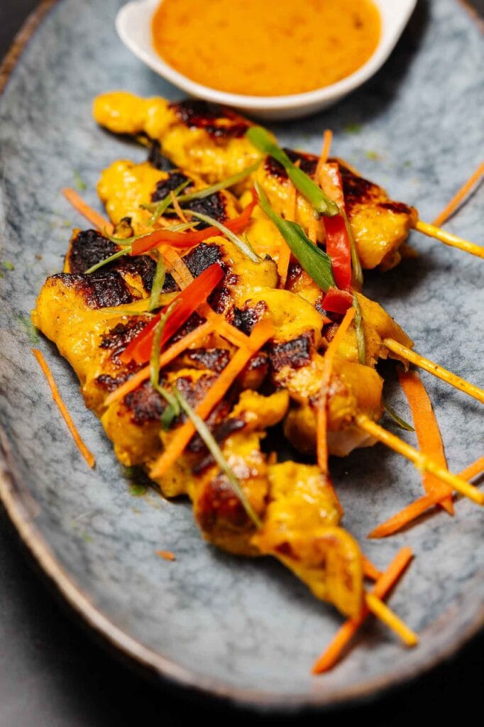 Grilled chicken satay skewers with vibrant vegetables served on a rustic plate, accompanied by a spicy dipping sauce, perfect for food photography and showcasing Asian-inspired cuisine.