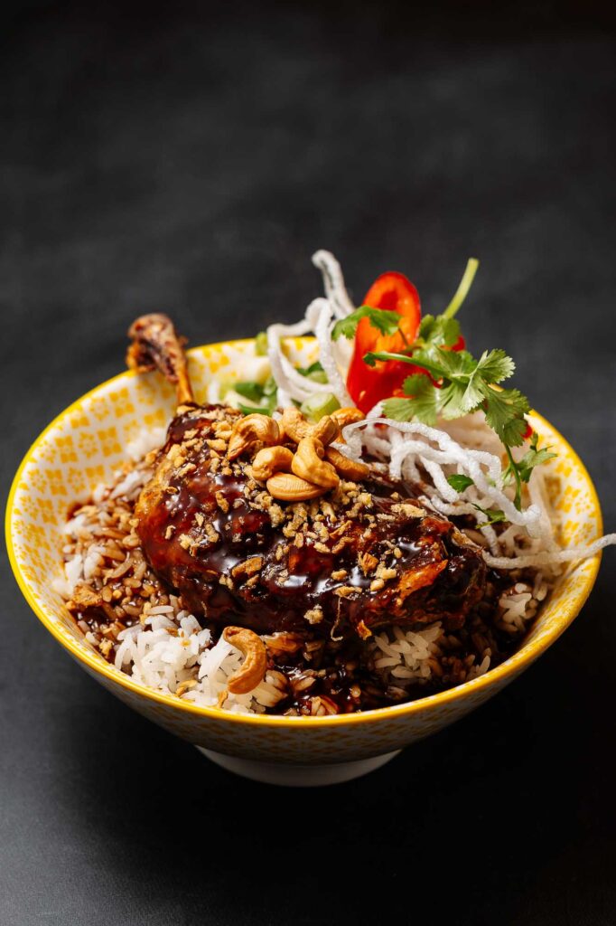 An appetising rice bowl featuring tender chicken glazed with rich sauce, topped with crunchy nuts, fresh herbs, and colourful vegetables, styled by Rutland Food Photographer.