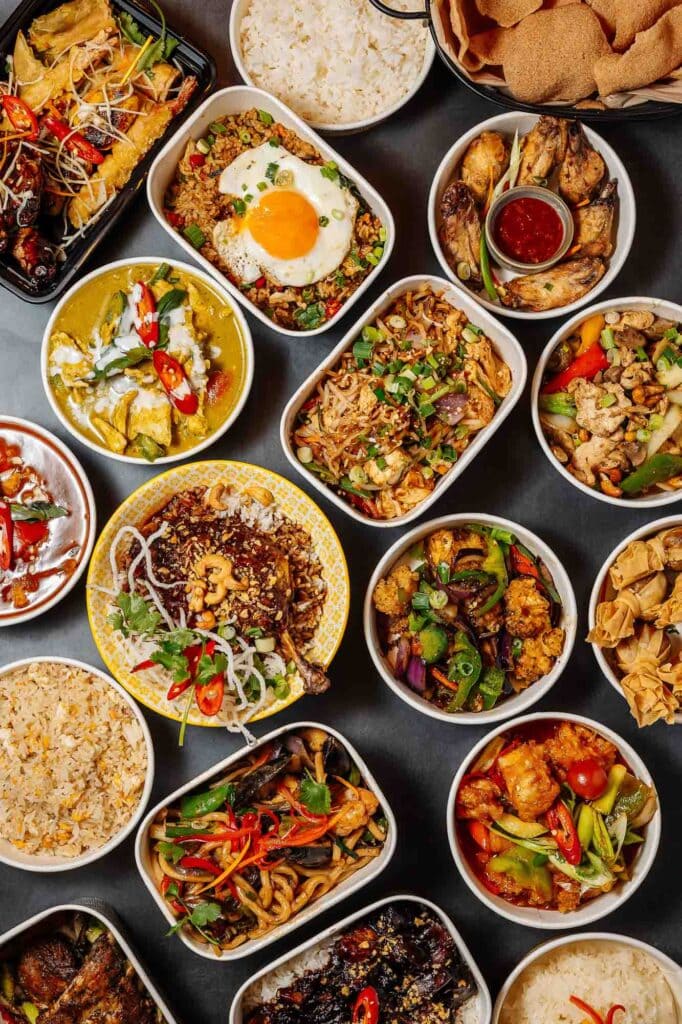 Vibrant Asian cuisine featuring a variety of dishes including rice, noodles, curries, and stir-fries, beautifully presented in white bowls on a black background, showcasing colourful ingredients and g.