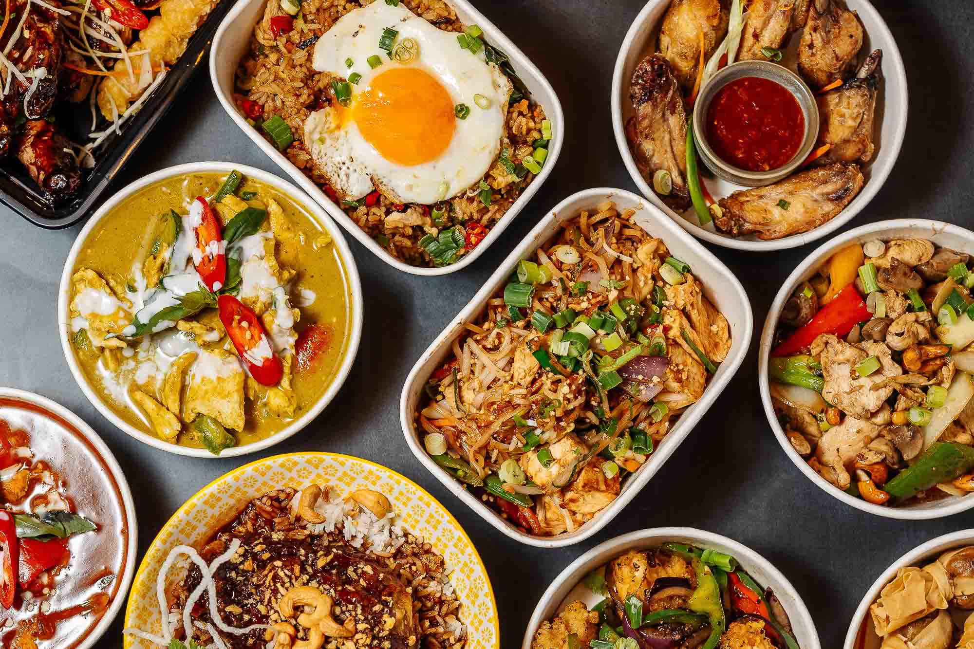 Colourful selection of Asian-inspired dishes served in white bowls, featuring rice, vegetables, meats, and sauces, showcasing diverse flavours and fresh ingredients.