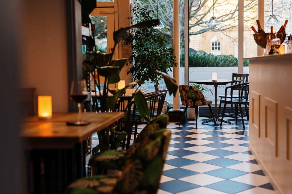 Interior of a Rutland café featuring checkered flooring, wooden furniture, and large windows allowing natural light, creating a warm and inviting atmosphere for diners.