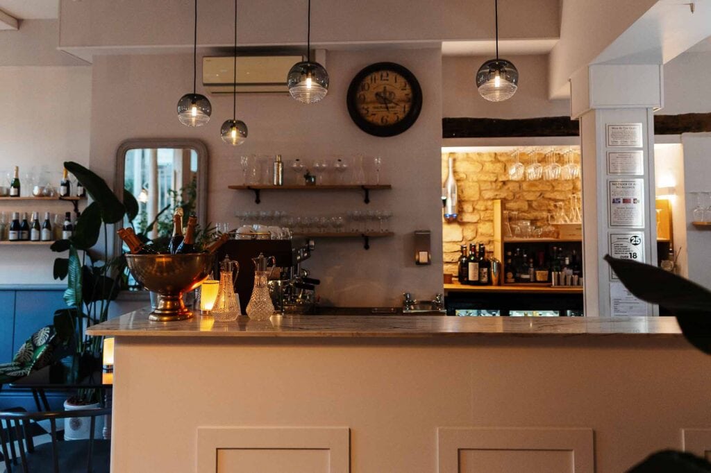 Interior shot of a stylish Rutland café showcasing a cozy bar area with warm lighting, decorative shelves, and a stone feature wall, perfect for food photography and hospitality branding.