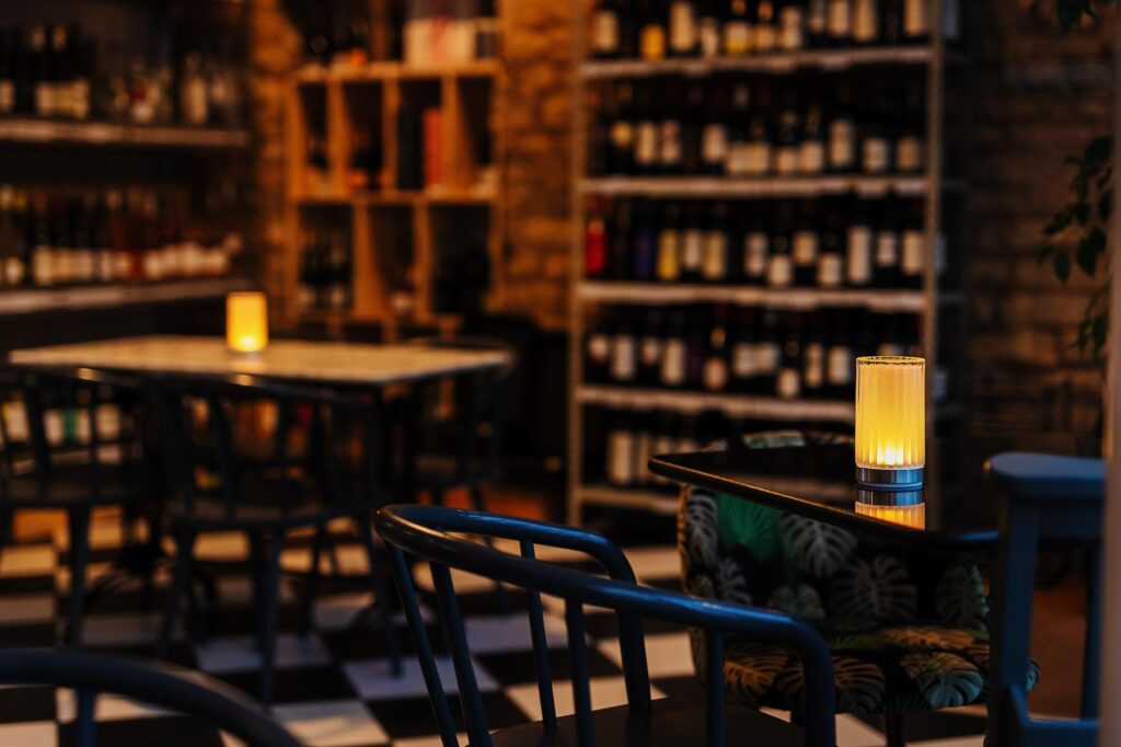 Stylish wine bar interior with warm lighting, wooden shelves filled with wine bottles, and cozy seating, perfect for wine tasting and socialising in a sophisticated setting.