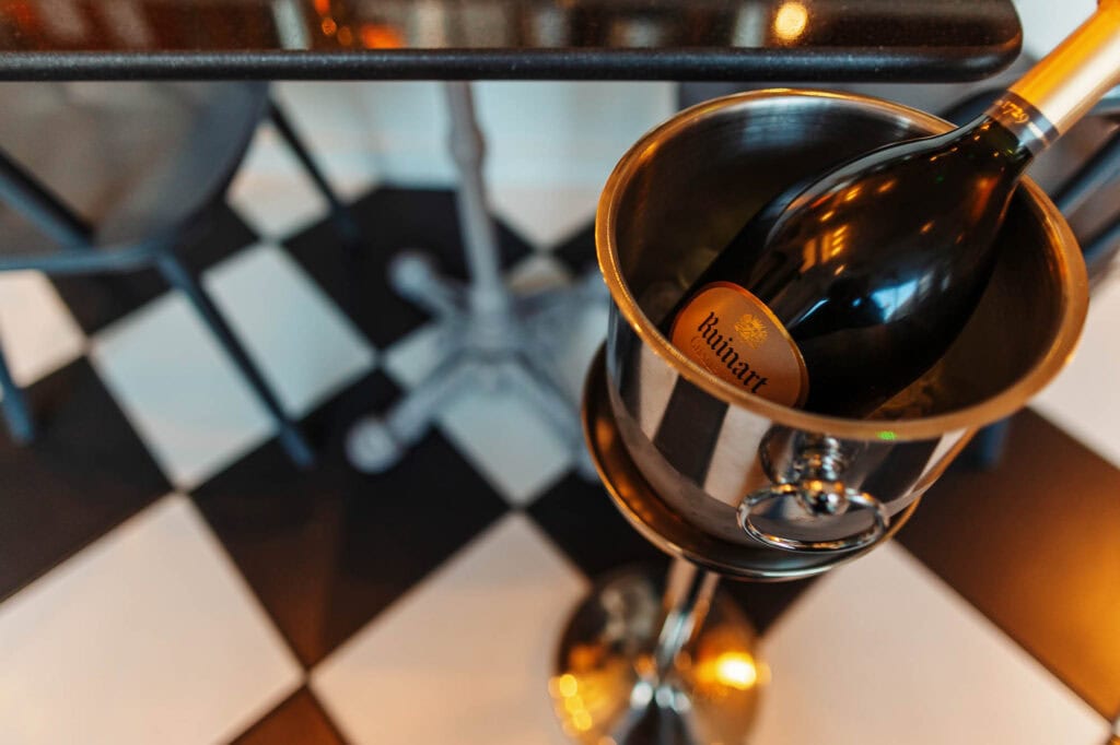 Elegant champagne bottle chilling in a silver ice bucket on a stylish black and white checkered floor, perfect for food photography and restaurant presentation.