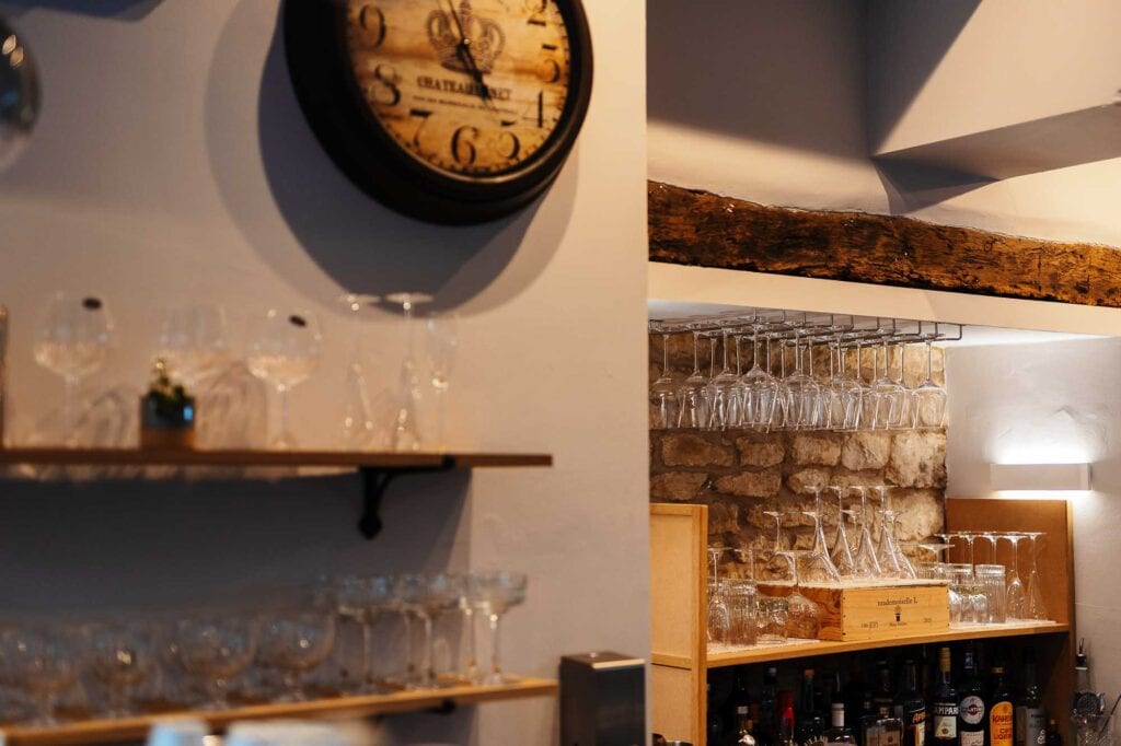 Interior shot of a rustic bar with wooden shelves stocked with glassware and bottles, featuring exposed brick walls and warm lighting, captured by a professional food photographer in Rutland.