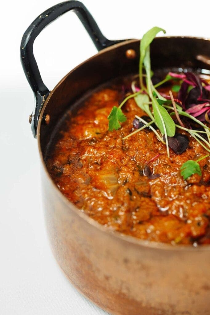 Delicious Indian stew with rich spices and fresh herbs served in a traditional copper pot, highlighting authentic flavours and vibrant presentation.