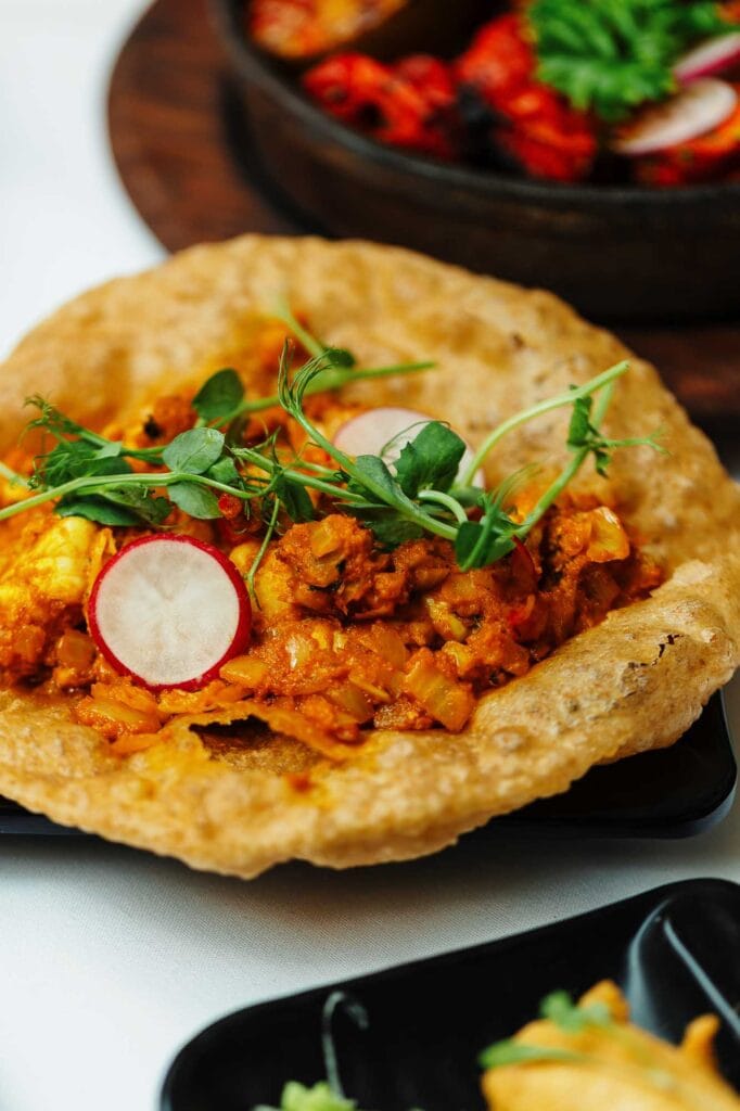 Delicious Indian dish featuring crispy bread topped with spiced minced meat, fresh radish slices, and microgreens, served as part of the Jashir menu at Oakham's Indian restaurant.