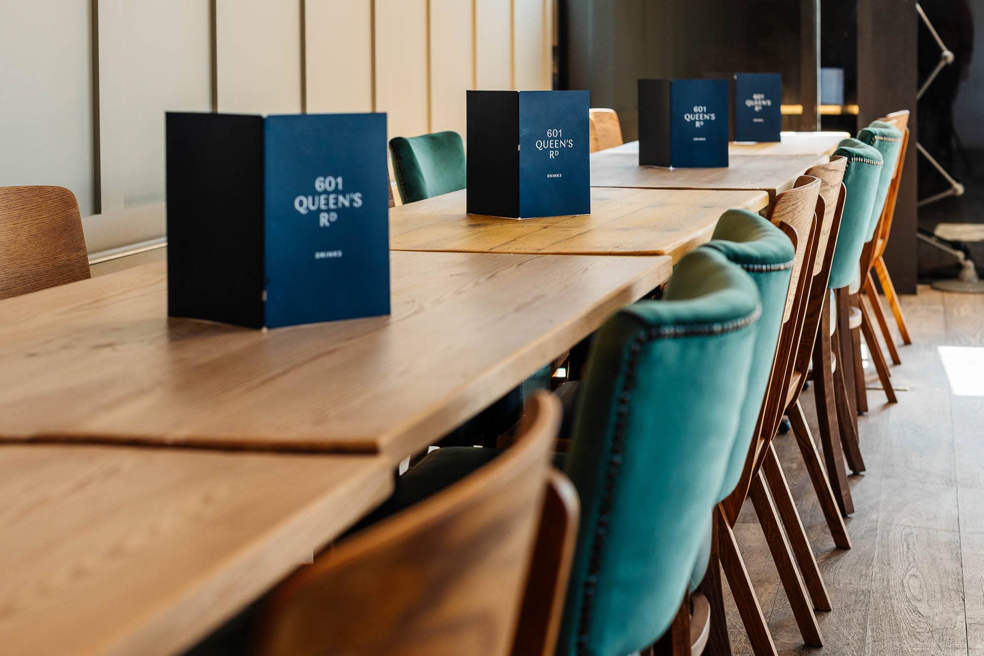 Elegant dining setup featuring a long wooden table with a mix of teal, brown, and beige chairs, each with a menu card, in a stylish restaurant environment.
