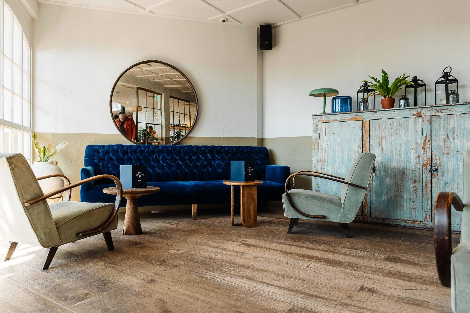 Elegant lounge featuring a velvet blue sofa, vintage armchairs, and rustic wooden furniture in a stylish, modern setting. Perfect for relaxing or casual meetings.