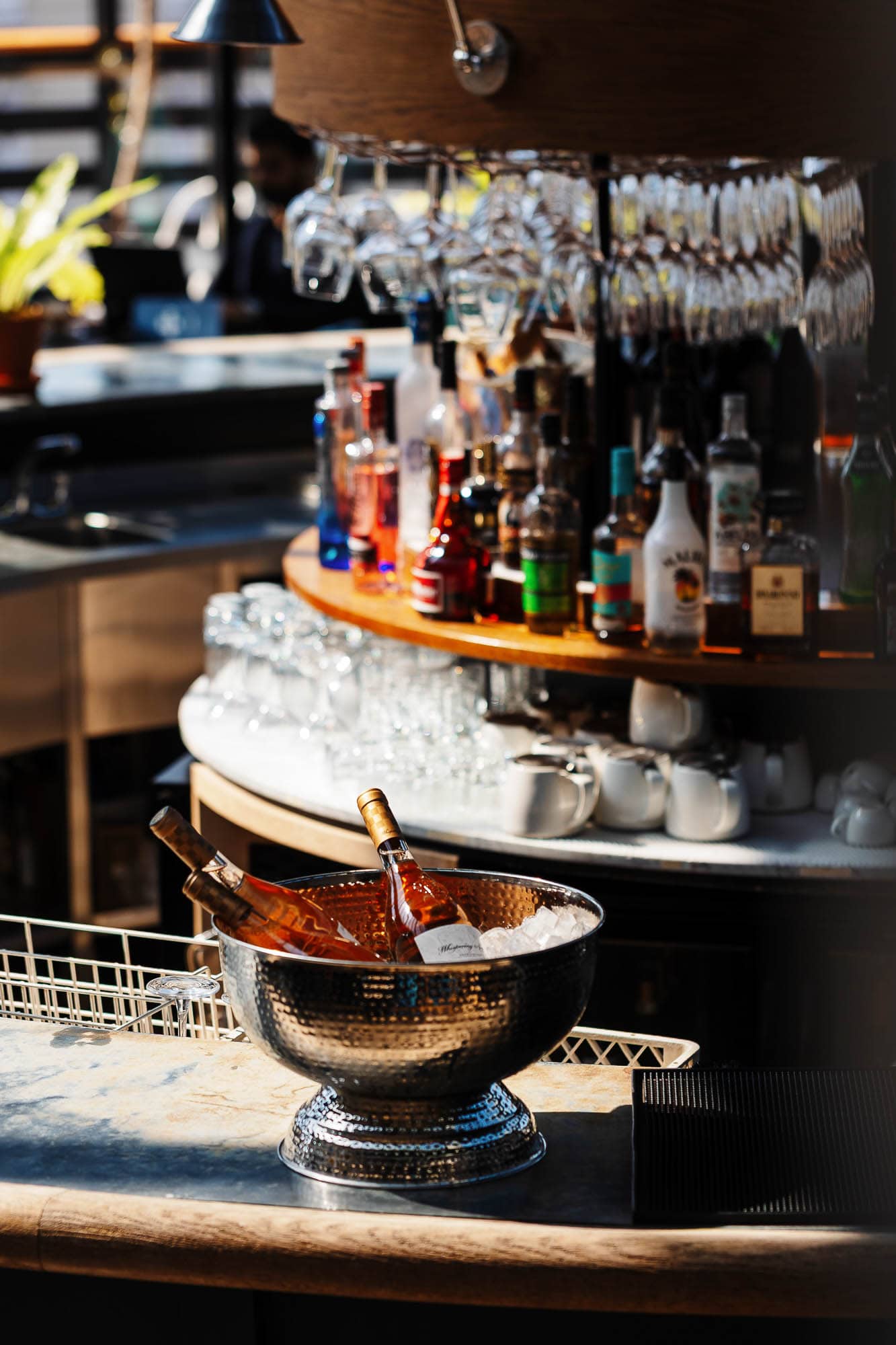Elegant bar setup showcasing a variety of colourful liquor bottles and hanging wine glasses in a stylish pub environment.