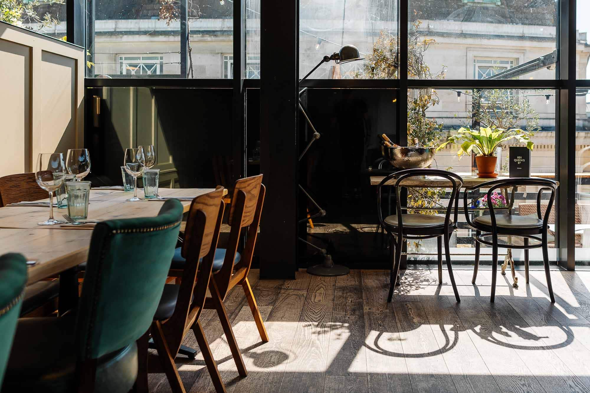 Elegant restaurant dining area with natural sunlight, stylish wooden and upholstered chairs, and a large window view of city buildings. Perfect for food photography showcasing inviting dining spaces.