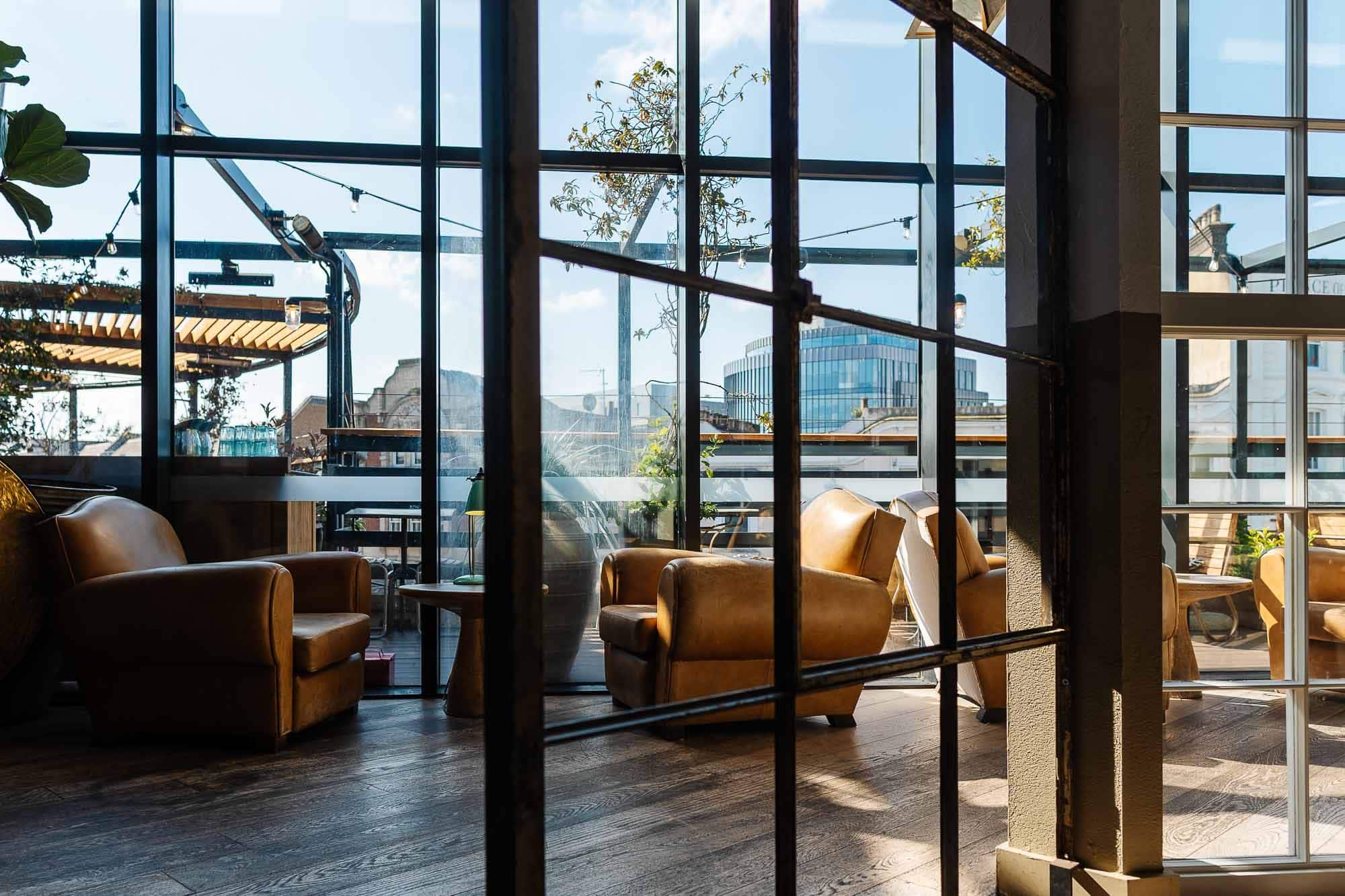 Bright lounge area with large floor-to-ceiling windows, leather armchairs, and a view of the city skyline, perfect for relaxing or casual meetings.