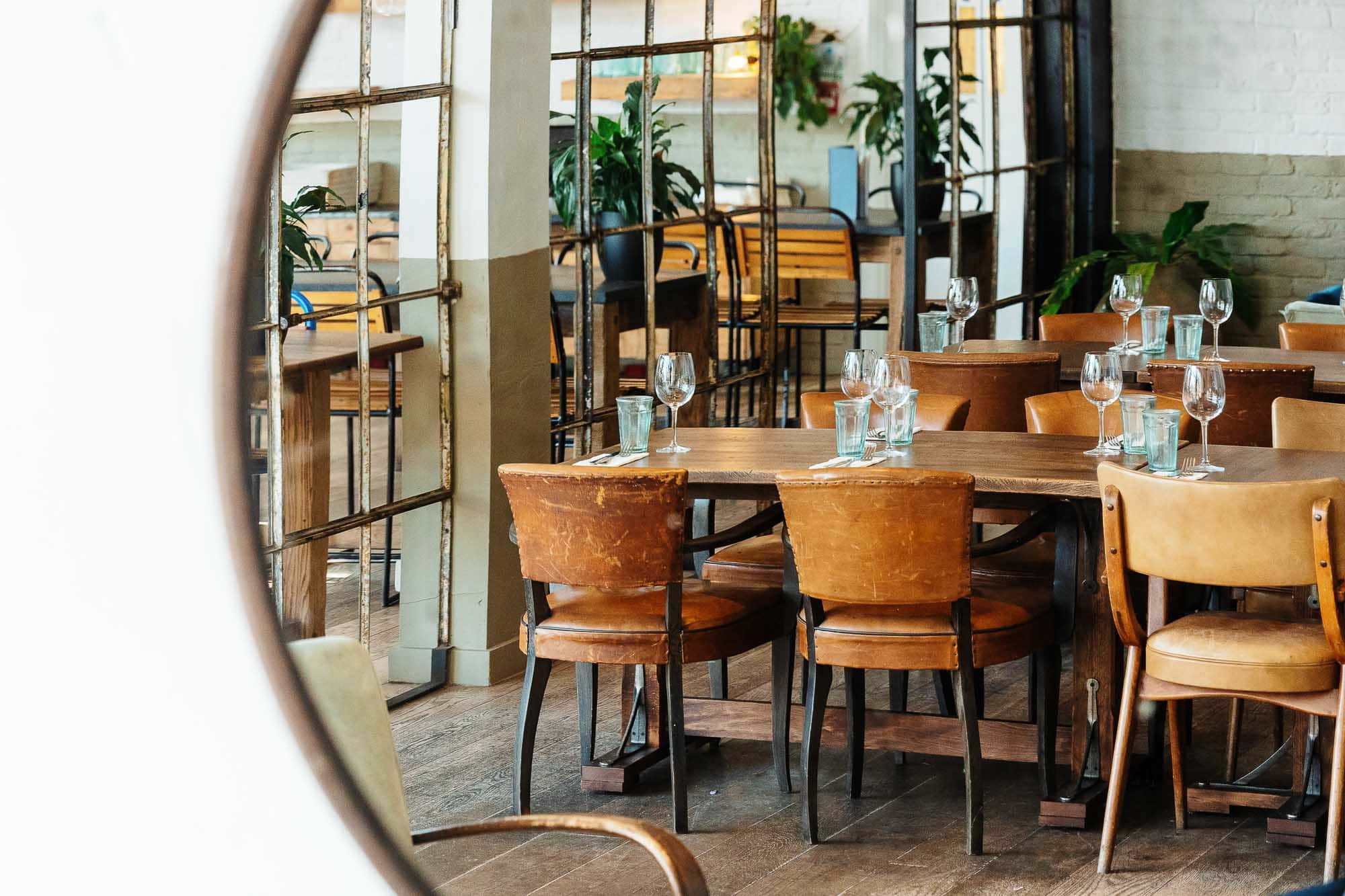 Modern rustic restaurant interior featuring wooden tables, leather chairs, and large windows with natural light, perfect for dining in a cosy, stylish setting.
