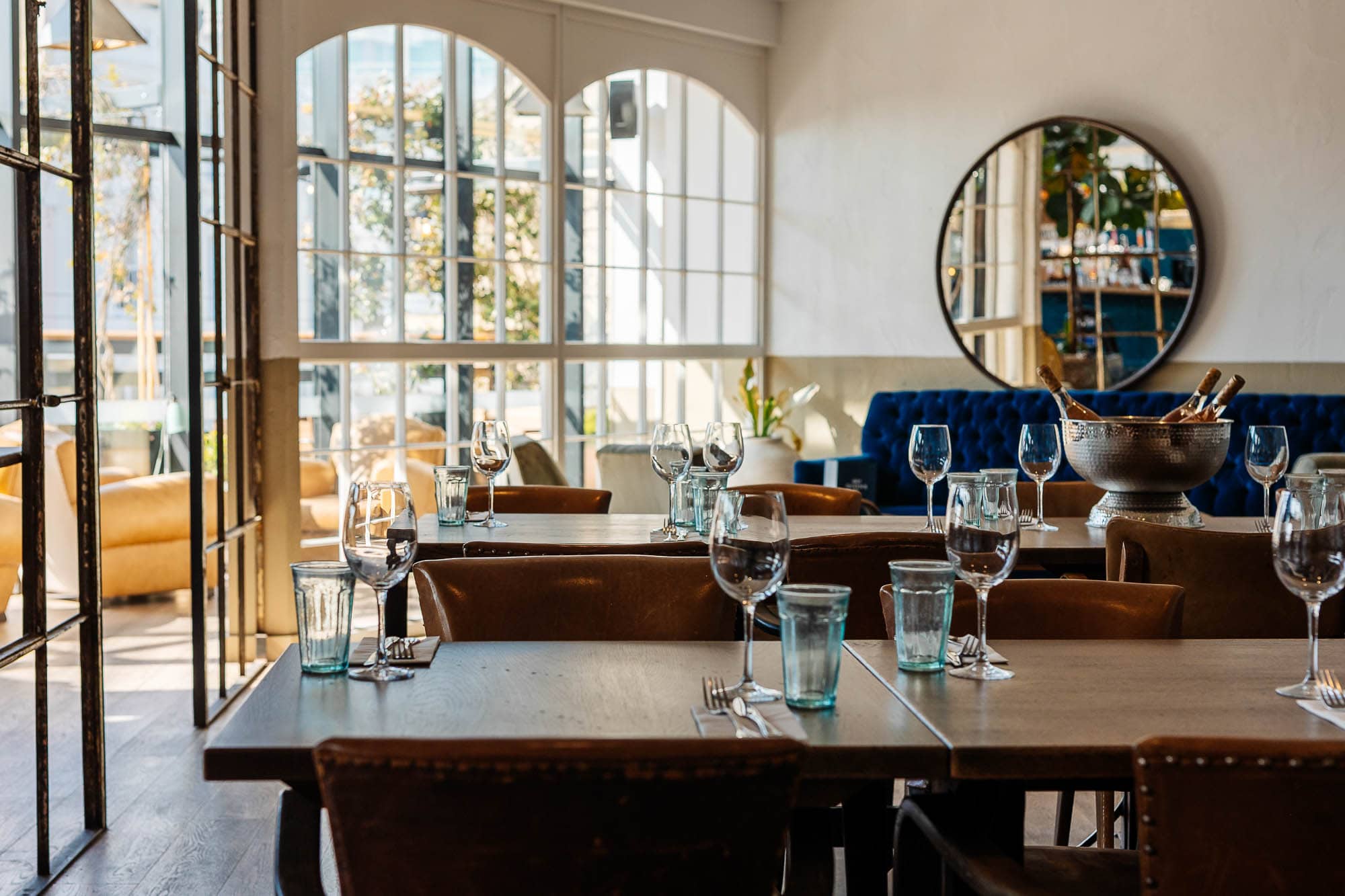 Stylish restaurant interior with large windows, wooden tables, and elegant glassware, perfect for food photography and showcasing dining ambiance.